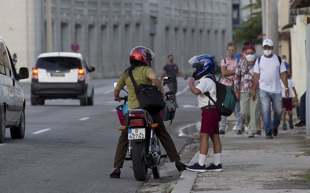 Personas caminan por la calle mientras un niño se baja de una moto.