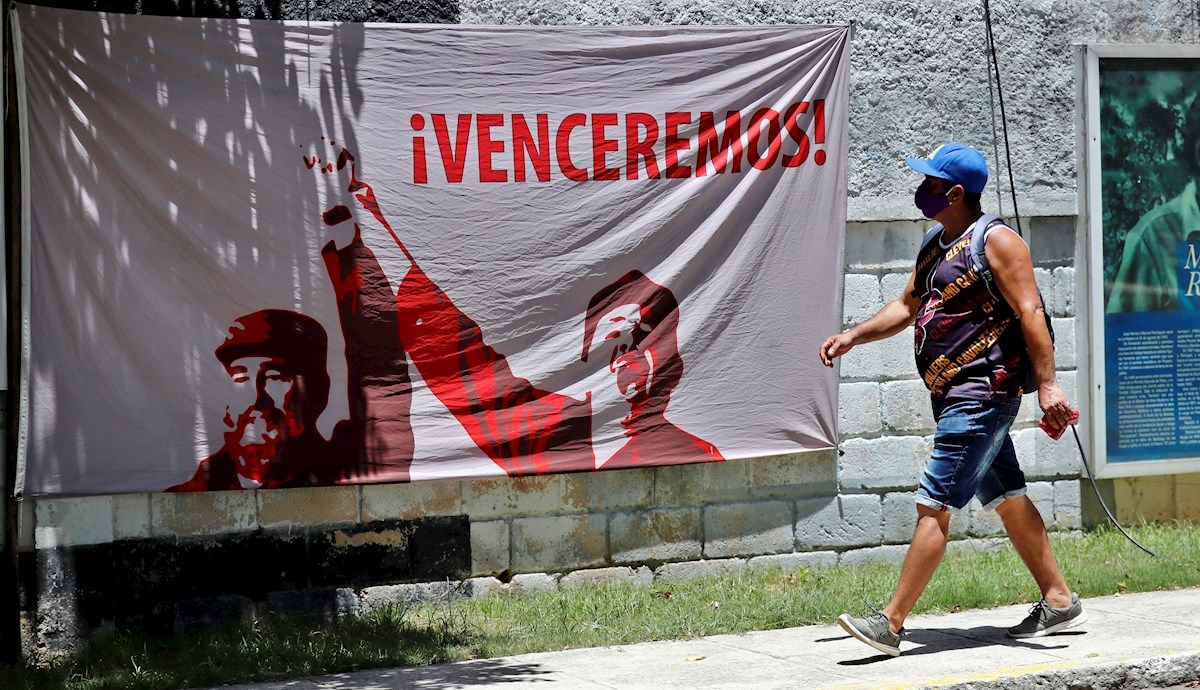 Un cubano camina por delante de un cartel de propaganda durante la pandemia.