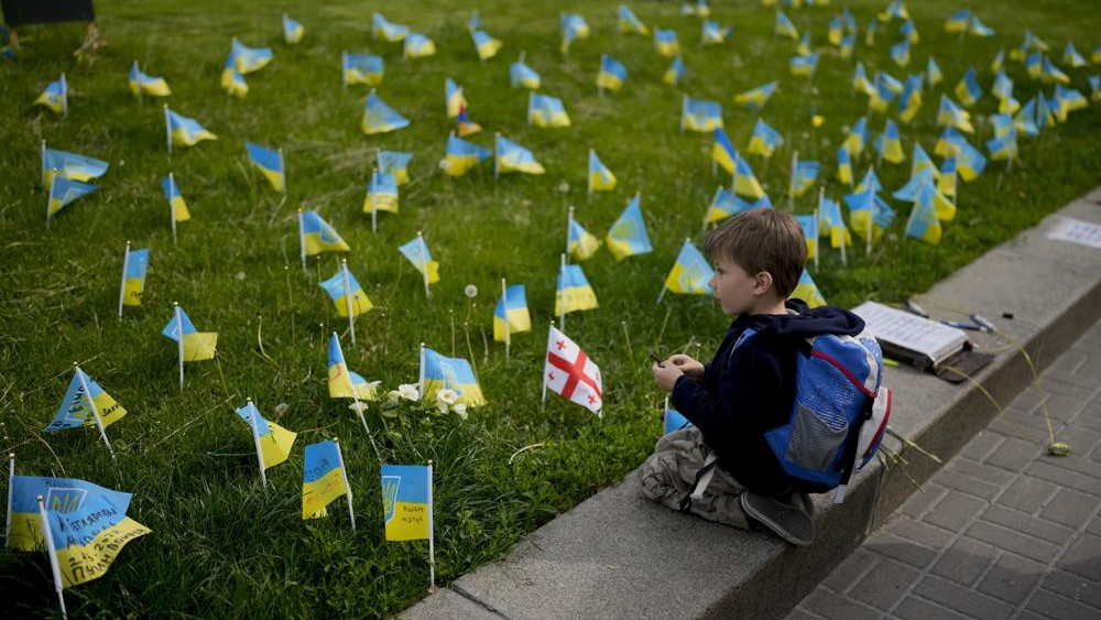 Un niño mira banderas en honor a soldados muertos en la guerra contra Rusia en el centro de Kiev, Ucrania, el lunes 23 de mayo de 2022.