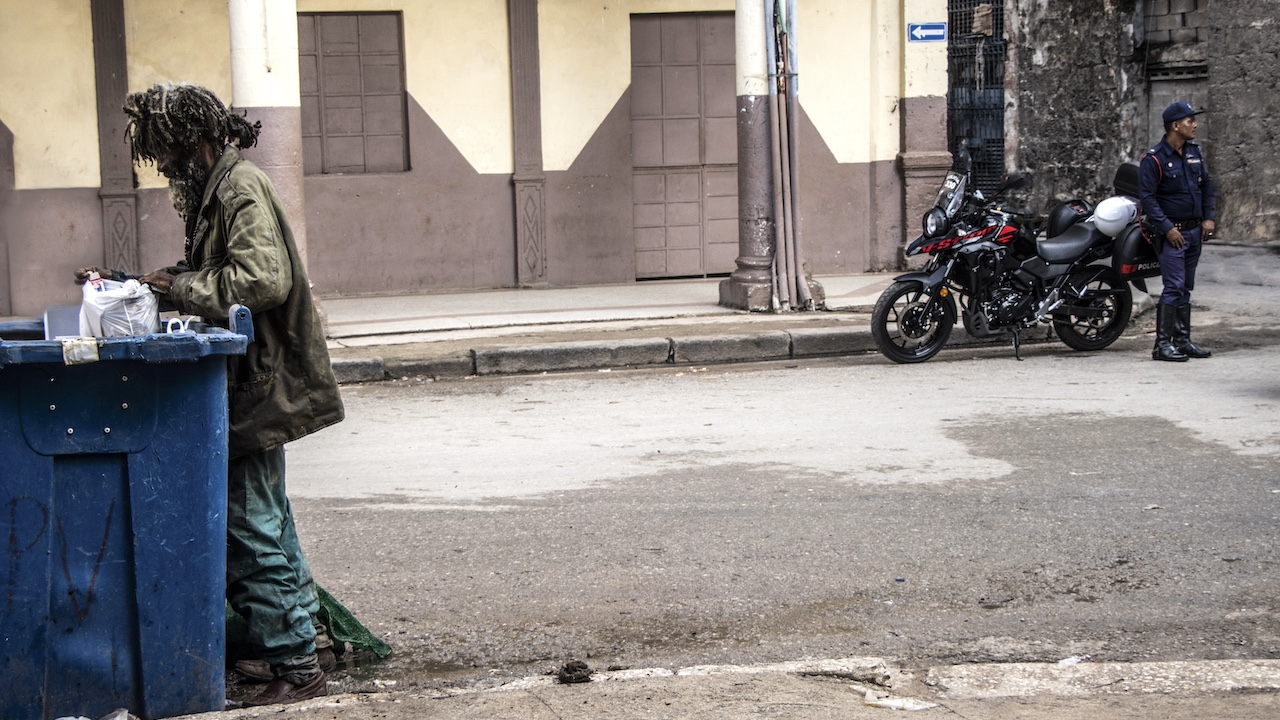 Un indigente buscando en la basura y un policía en La Habana.