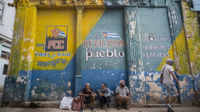 Ancianos cubanos en La Habana frente a una pared con lemas propagandísticos.